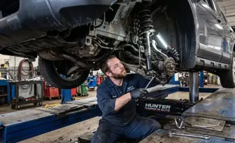A mechanic inspecting struts and suspension under a raised car